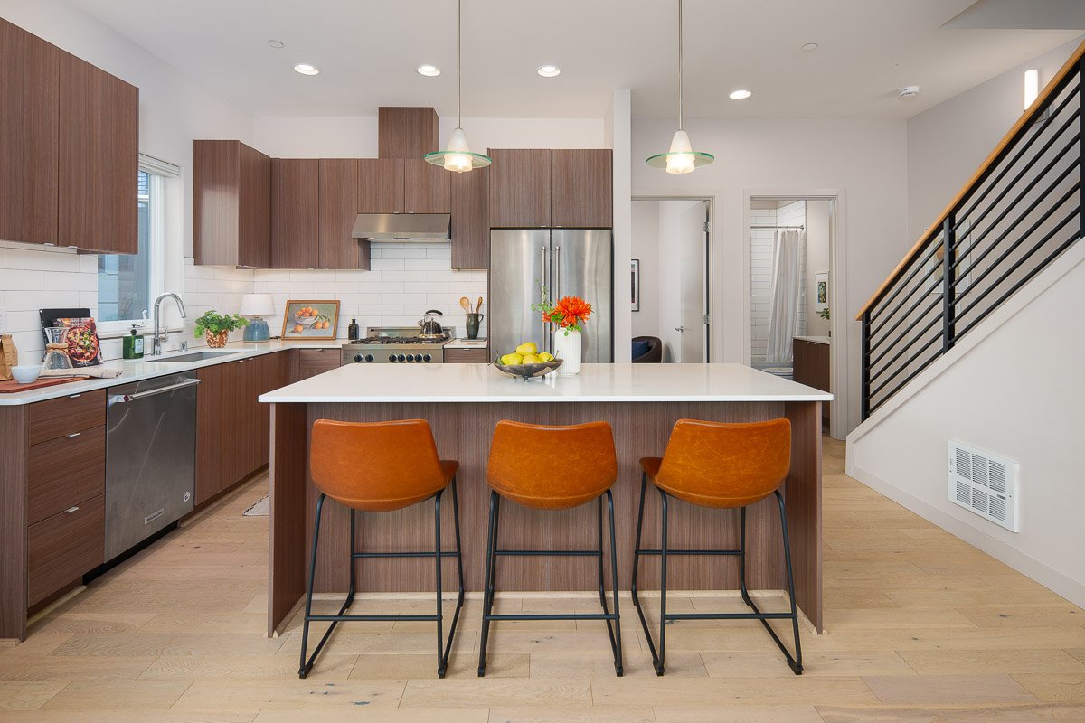 Professional real estate photography of a modern Seattle townhouse kitchen with wood cabinetry, large island, stainless steel appliances, and contemporary finishes.