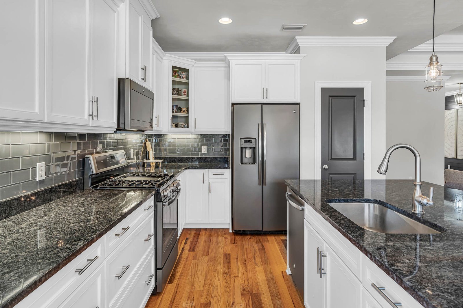 Professional real estate photography of a modern Seattle kitchen with white cabinetry, granite countertops, stainless steel appliances, and hardwood floors.