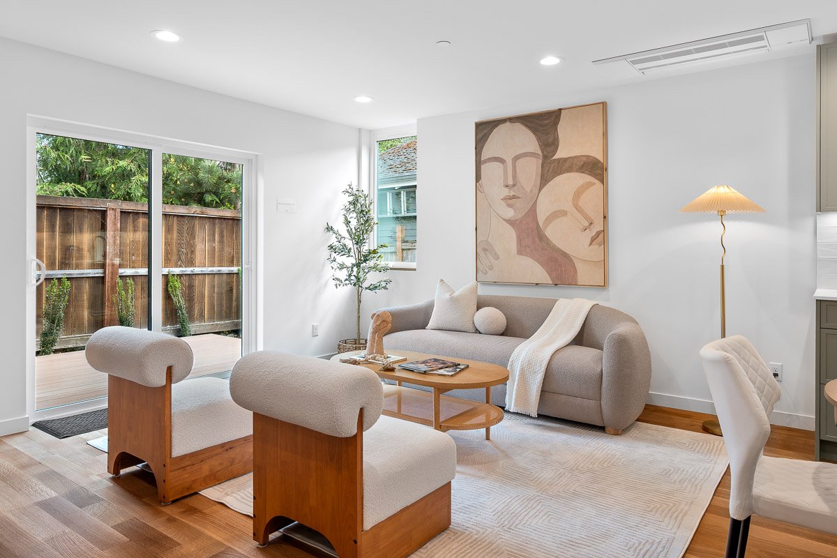 Professional real estate photography of a bright Seattle living room with modern staging, warm wood floors, large windows, and direct access to a private patio.