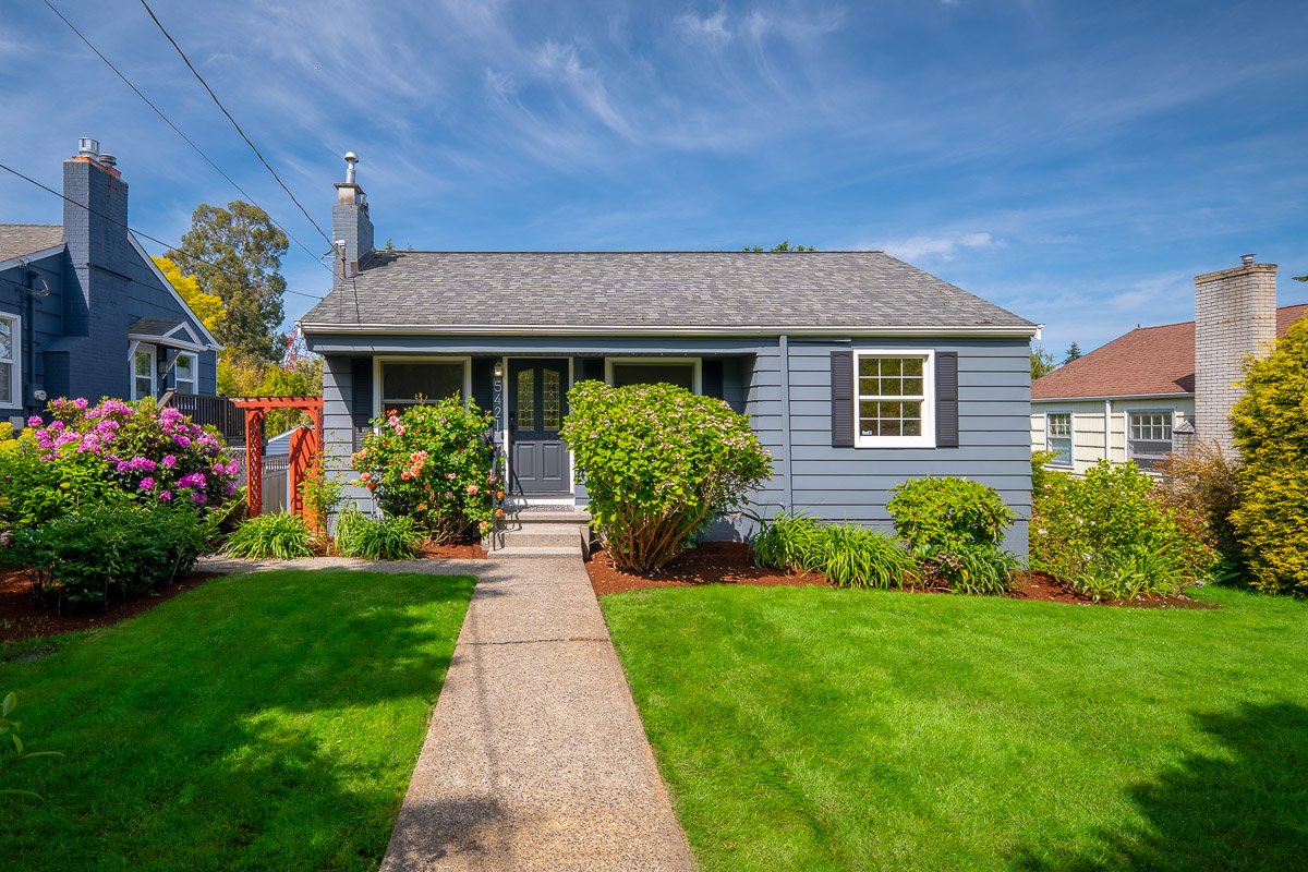 Professional real estate exterior photography of a landscaped Seattle home with bright curb appeal, blue skies, and a manicured front yard.