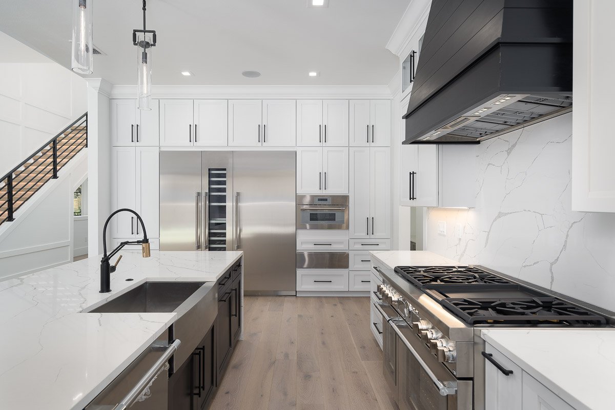 Professional real estate photography of a luxury Seattle kitchen with white cabinetry, quartz countertops, high-end stainless steel appliances, and modern black accents.