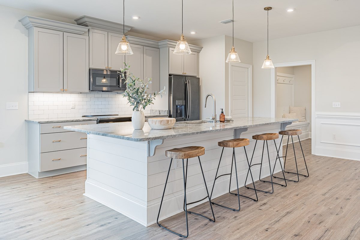 Professional real estate photography of a bright Seattle kitchen with a large stone island, gray cabinetry, pendant lighting, stainless steel appliances, and modern farmhouse details.